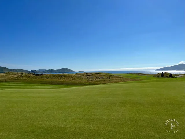 A green and flagstick at Hogs Head, with sand in front and the mountains beyond.