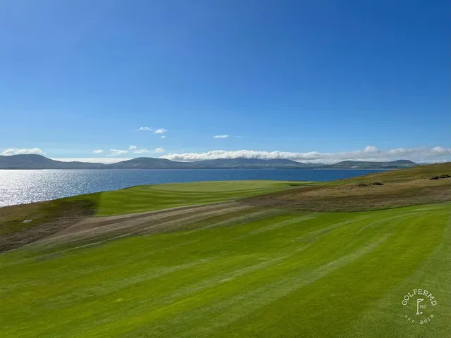 A golfer hitting a shot from the fairway at Hogs Head, with the mountains ahead.