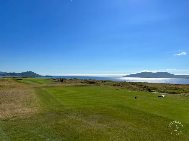A green and flagstick at Hogs Head, with sand short of the green and the water beyond.