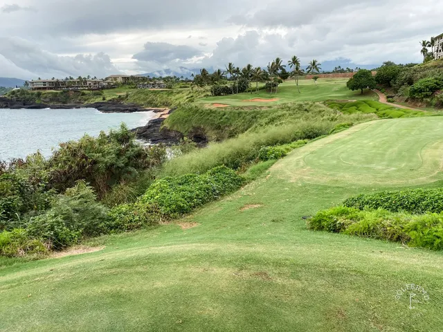 A golfer hitting a shot at Hōkūala, with the fairway and ocean ahead.