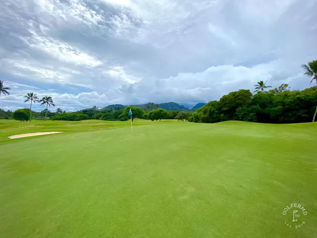 A green and flagstick at the Ocean Course, seen across a sand bunker, with the water on the horizon.