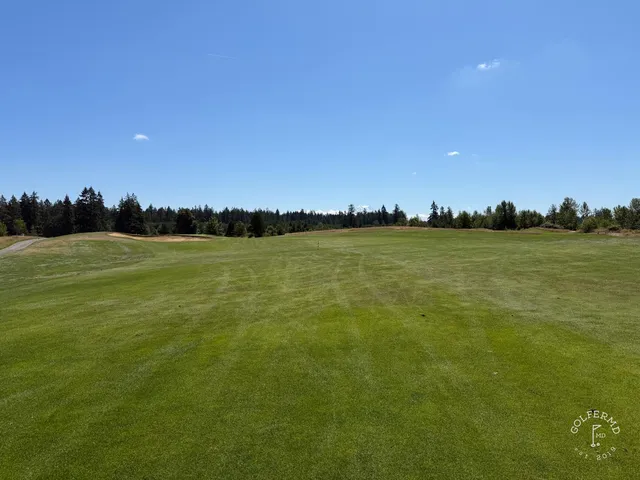 A wide view at The Home Course, with the fairway and a tree line in the distance.