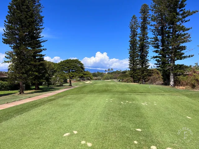A green and flagstick at the Kai Course, with a sand bunker in the foreground and the ocean behind the hole.
