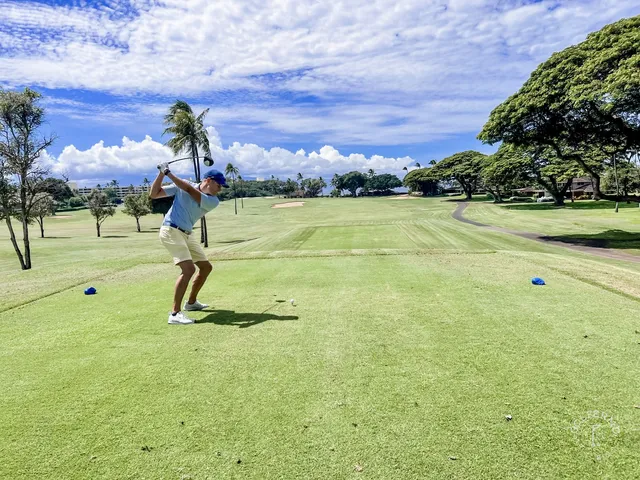 A green and flagstick at the Royal Course, with a sand bunker in front and the ocean behind the hole.