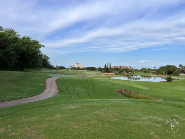 A golfer hitting a shot from the fairway at Ko Olina, with palm trees and the ocean behind the hole.