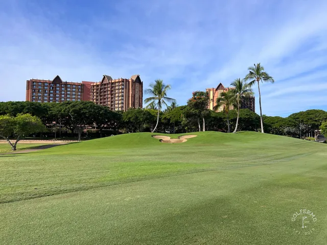 A green and flagstick at Ko Olina, with a pond in front and palm trees around the hole.
