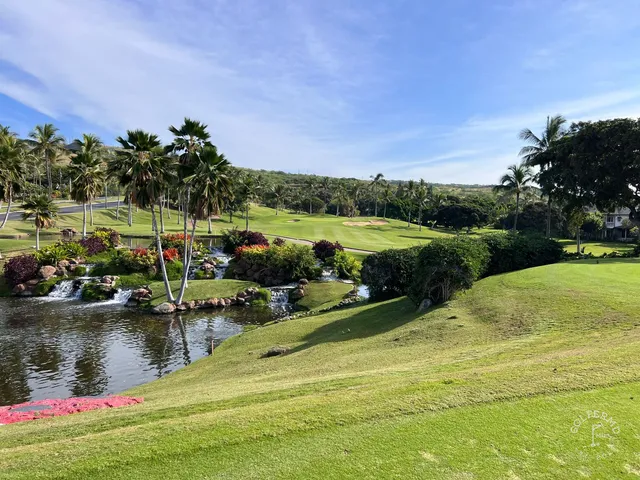 A green and flagstick at Ko Olina, seen across a pond, with the ocean on the horizon.