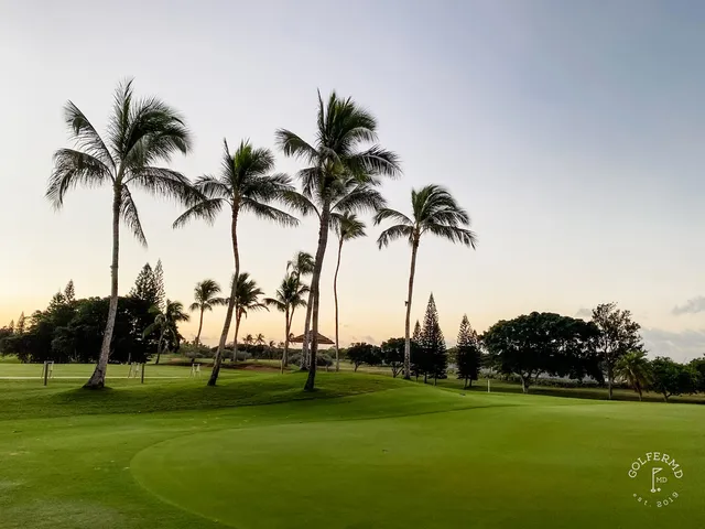 A wider view of a fairway at Ko Olina, with palm trees, a sand bunker, and the ocean in the distance.