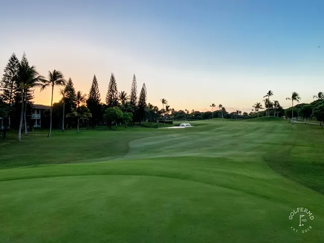 A golfer hitting a shot at Ko Olina, with palm trees and the ocean behind the hole.