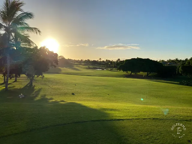 A golfer putting on a green at Ko Olina, with the ocean and a rocky shore behind the hole.