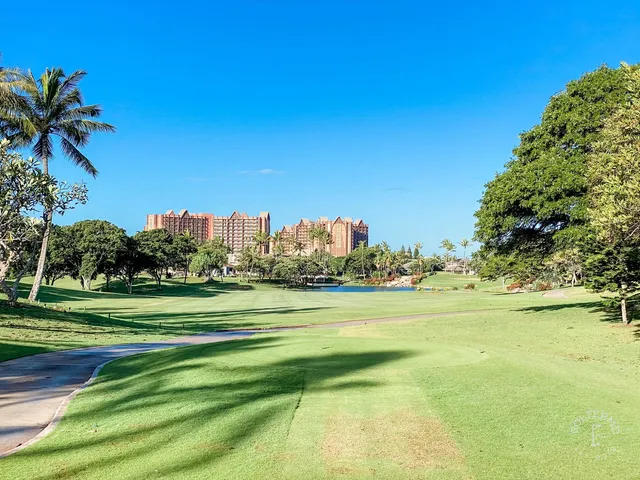 A fairway and green at Ko Olina, with a pond on the right and palm trees along the water.