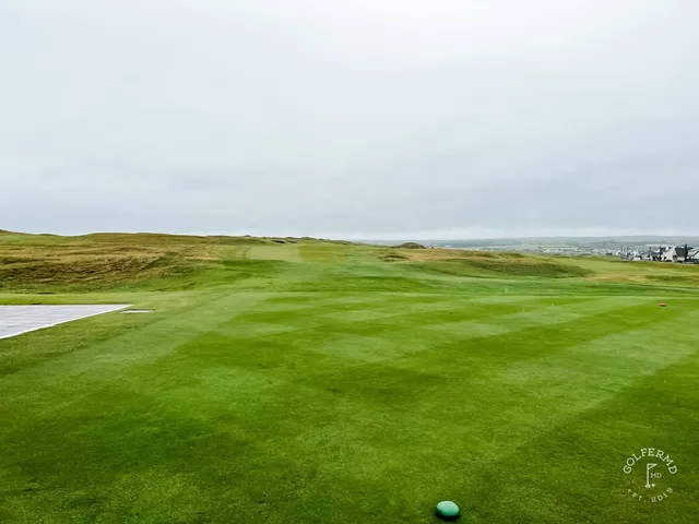 A green and flagstick at Lahinch, with a bunker in front and the ocean behind the hole.