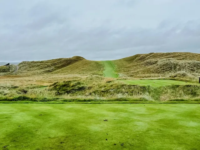 A golfer hitting a shot at Lahinch, with the fairway and the ocean ahead.