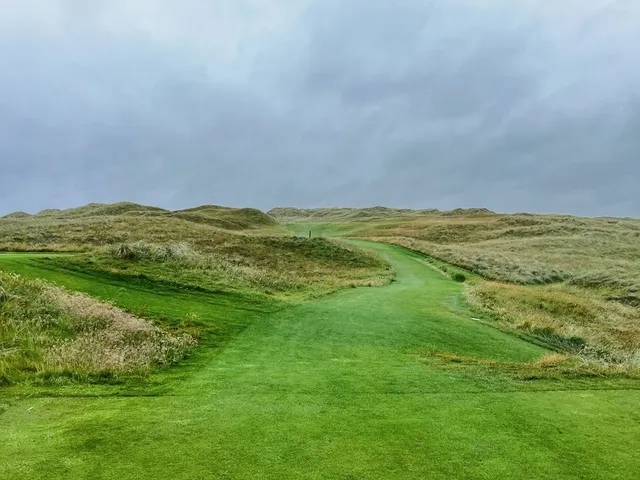 A golfer putting on a green at Lahinch, with the ocean beyond the hole.