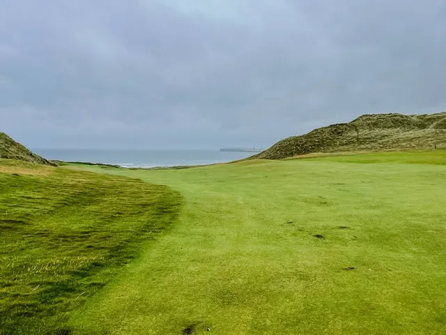 A close view of a green and flagstick at Lahinch, with the water behind it.