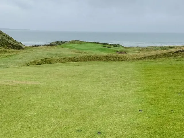 A fairway and green at Lahinch, with a bunker in the foreground and the ocean beyond.