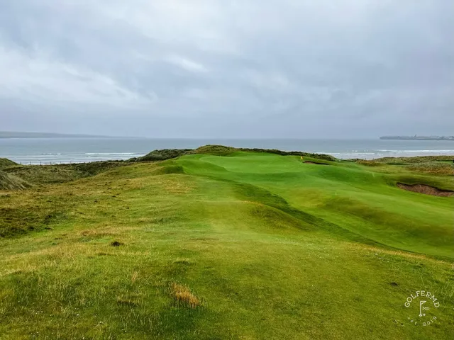A green and flagstick at Lahinch, seen from a rise, with the ocean behind the hole.