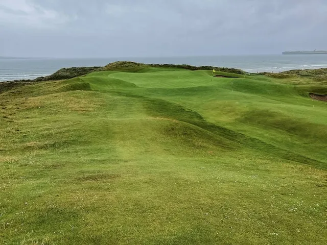 A close view of a flagstick at Lahinch, with the Atlantic behind the green.