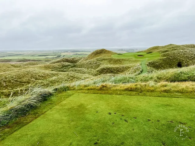 A green and flagstick at Lahinch, with a deep bunker in front and the water beyond.