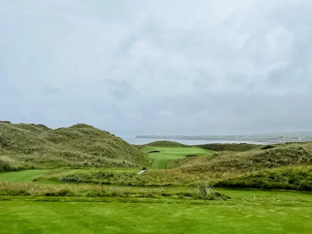 A green and flagstick at Lahinch, with sand in front and the village beyond.