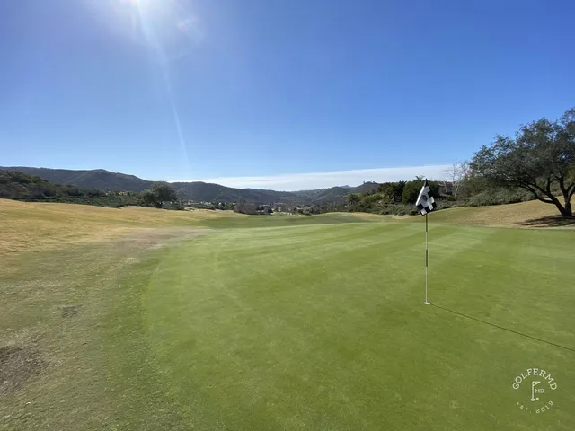 A green and flagstick at Maderas Golf Club, with a bunker in front and hills behind.