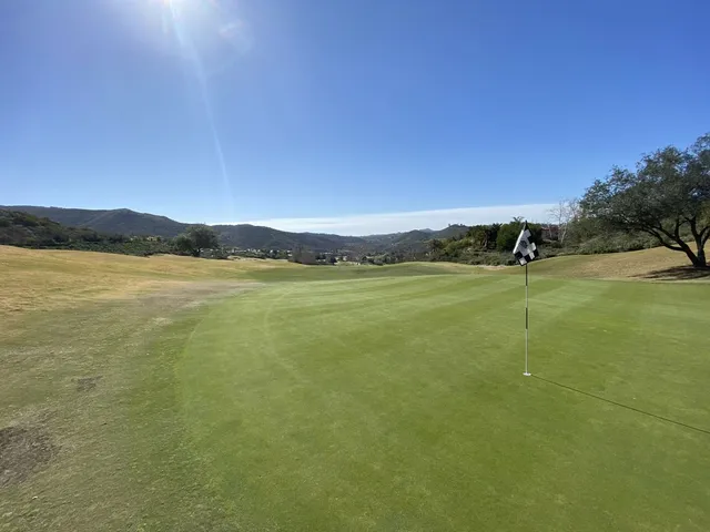 A fairway dropping toward a green at Maderas Golf Club, with hills on both sides.