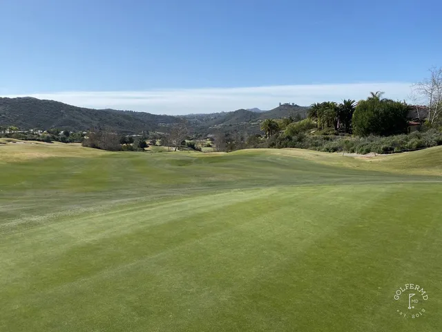 A green and flagstick in a valley at Maderas Golf Club, with a creek and trees beside the hole.