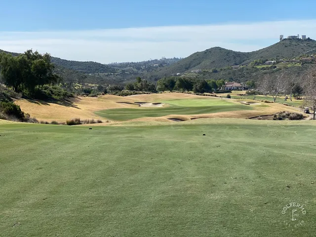 A green and flagstick at Maderas Golf Club, with a bunker in front and hills behind the hole.