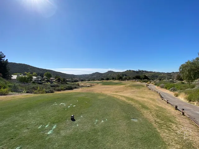 A green and flagstick at Maderas Golf Club, with a pond in front and hills behind the hole.