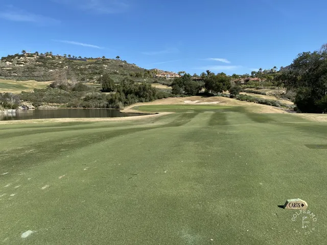 A fairway and green at Maderas Golf Club, with a pond beside the hole and hills beyond.