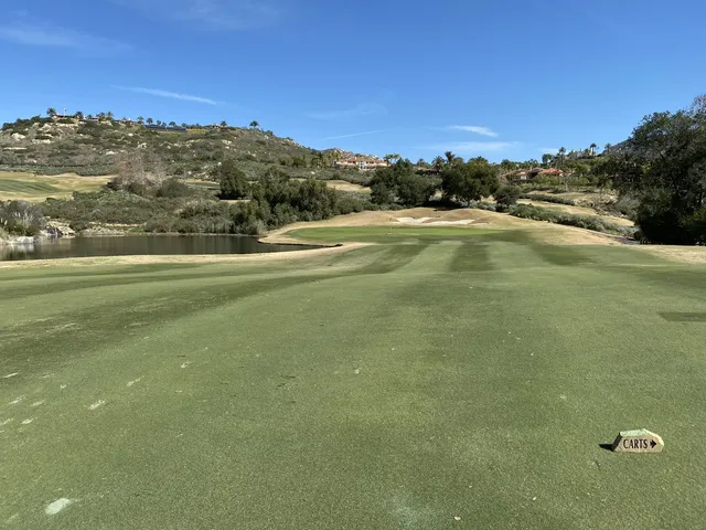 A green and flagstick beside a pond at Maderas Golf Club, seen from a rise.