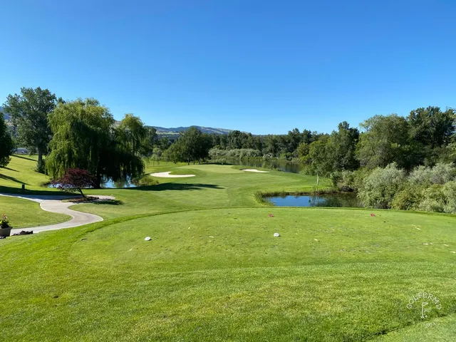 A green and flagstick at Missoula Country Club, with a bunker in front and the mountains beyond.