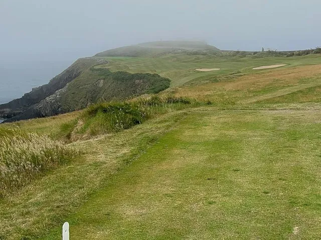 A green and flagstick at Old Head, with the ocean far below.