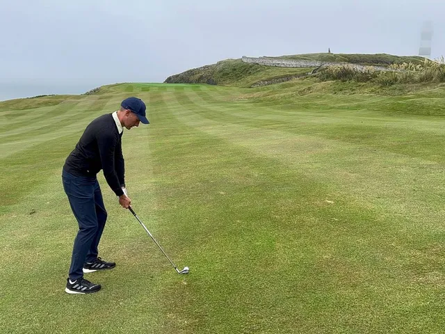 A golfer hitting a shot at Old Head, with the cliff edge and the ocean ahead.