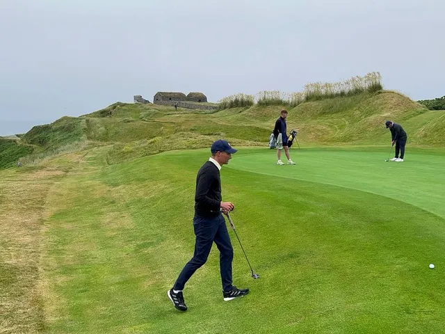 A green and flagstick at Old Head, seen from a rise, with the water behind the hole.
