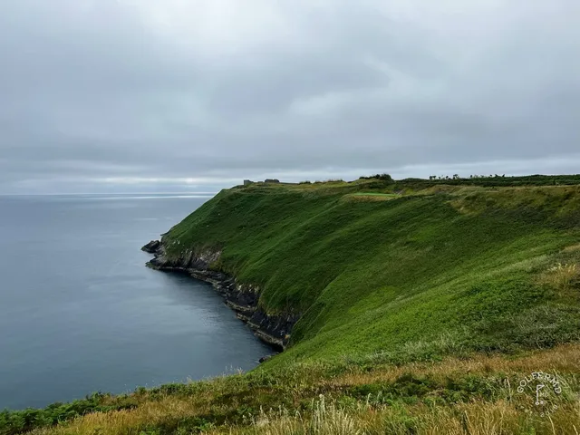 A golfer hitting a shot from the cliff edge at Old Head, with the water ahead.