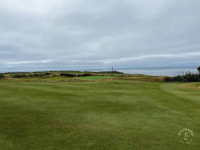 A green and flagstick at Old Head, with sand in front and the ocean on the horizon.