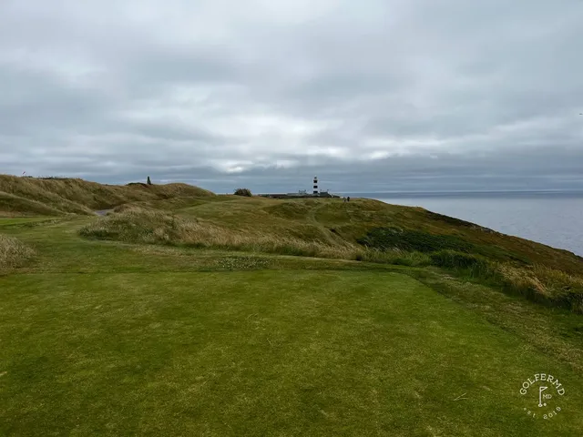 A green and flagstick at Old Head, seen from the tee, with the ocean behind the hole.