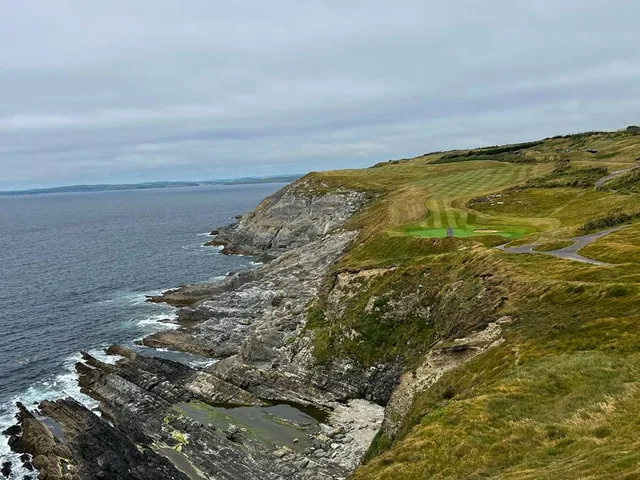 A golfer hitting a shot from the fairway at Old Head, with the lighthouse ahead.