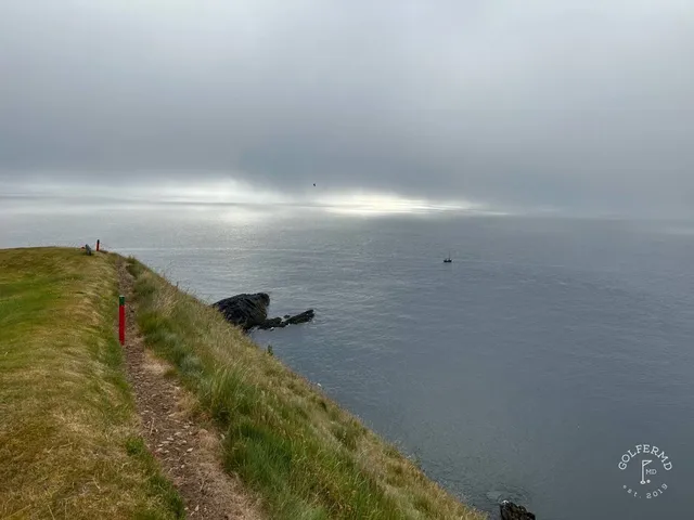 A golfer hitting a shot at Old Head, with the headland and the water ahead.