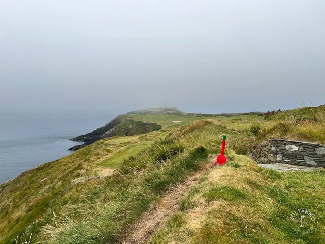 A green and flagstick at Old Head, with sand short of the green and the ocean beyond.