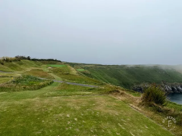 A green and flagstick at Old Head, with a bunker in front and the ocean behind the hole.