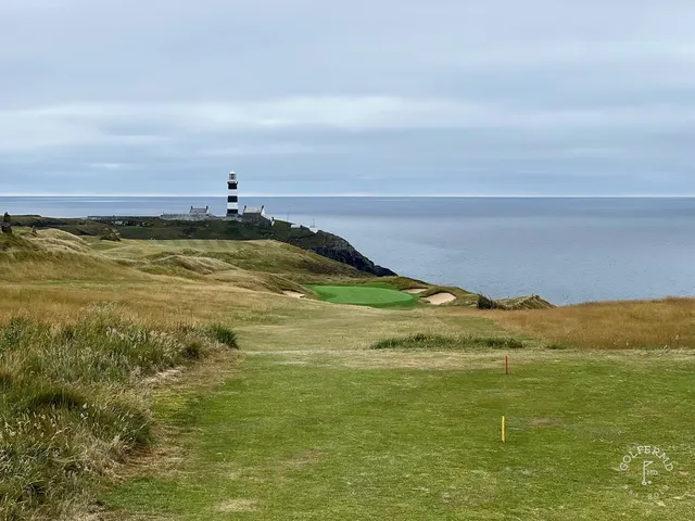 A green and flagstick at Old Head, seen across a bunker, with the water below.