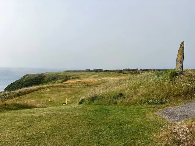 A golfer hitting from the rough at Old Head, with the ocean beyond.