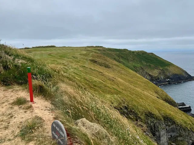 A green and flagstick at Old Head in the wind, with the ocean on the horizon.