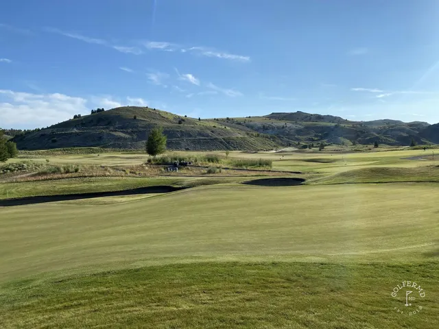 A golfer putting on a green at Old Works, with the mountains behind the hole.