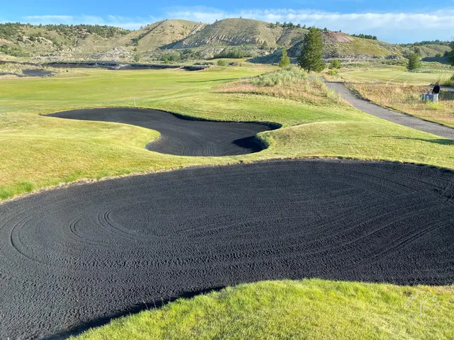 A close view of a green and flagstick at Old Works, with black sand around the green.