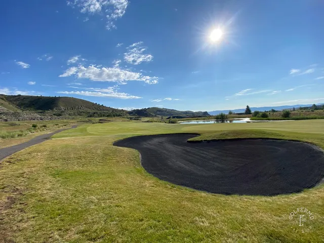 A green and flagstick at Old Works, framed by black bunkers and the mountains.