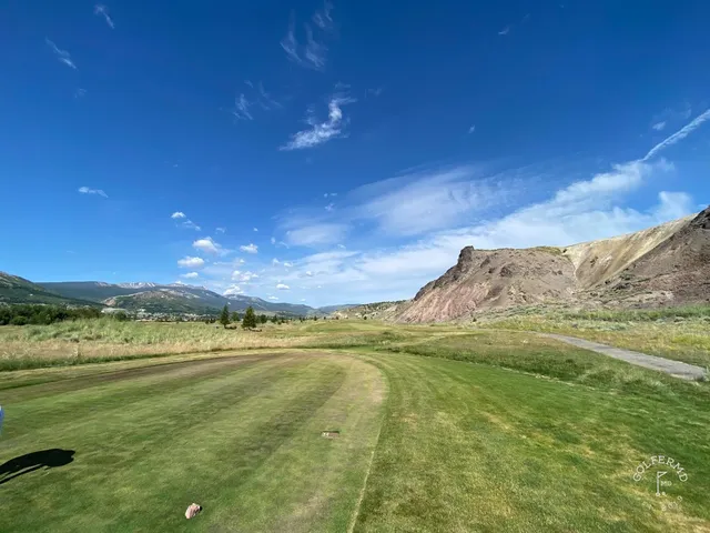 A golfer putting at Old Works, with black sand and the mountains behind the green.