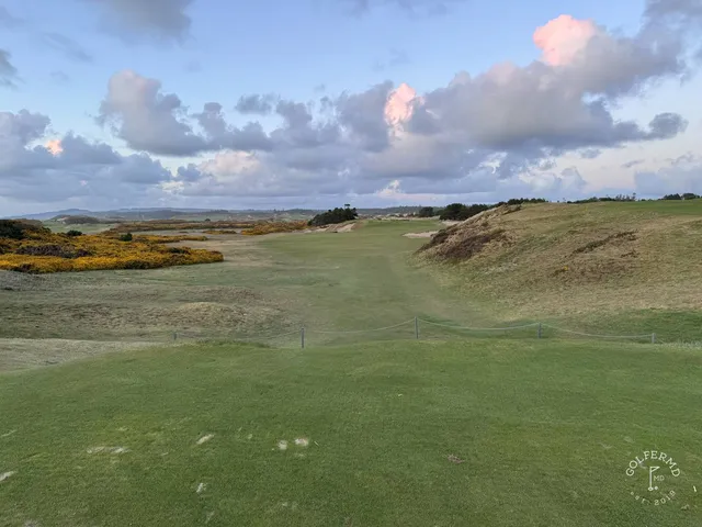 A green and flagstick at Pacific Dunes, with a bunker in front and the ocean behind the hole.